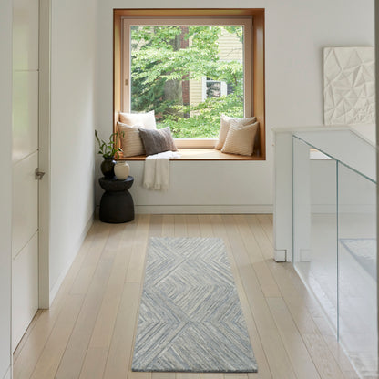 Bright hallway with pale wood floors, built-in window seat with cushions, blue-gray chevron runner rug, greenery outside window.