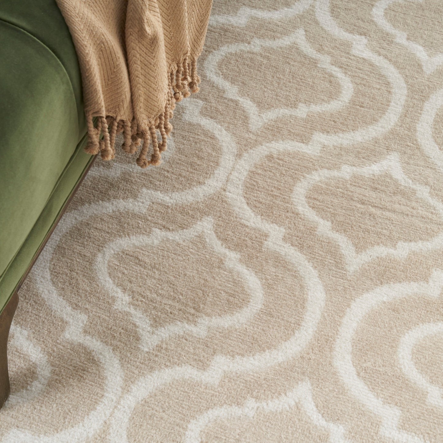 Beige and cream trellis-pattern rug with soft pile beside olive-green sofa and a tan fringed throw.