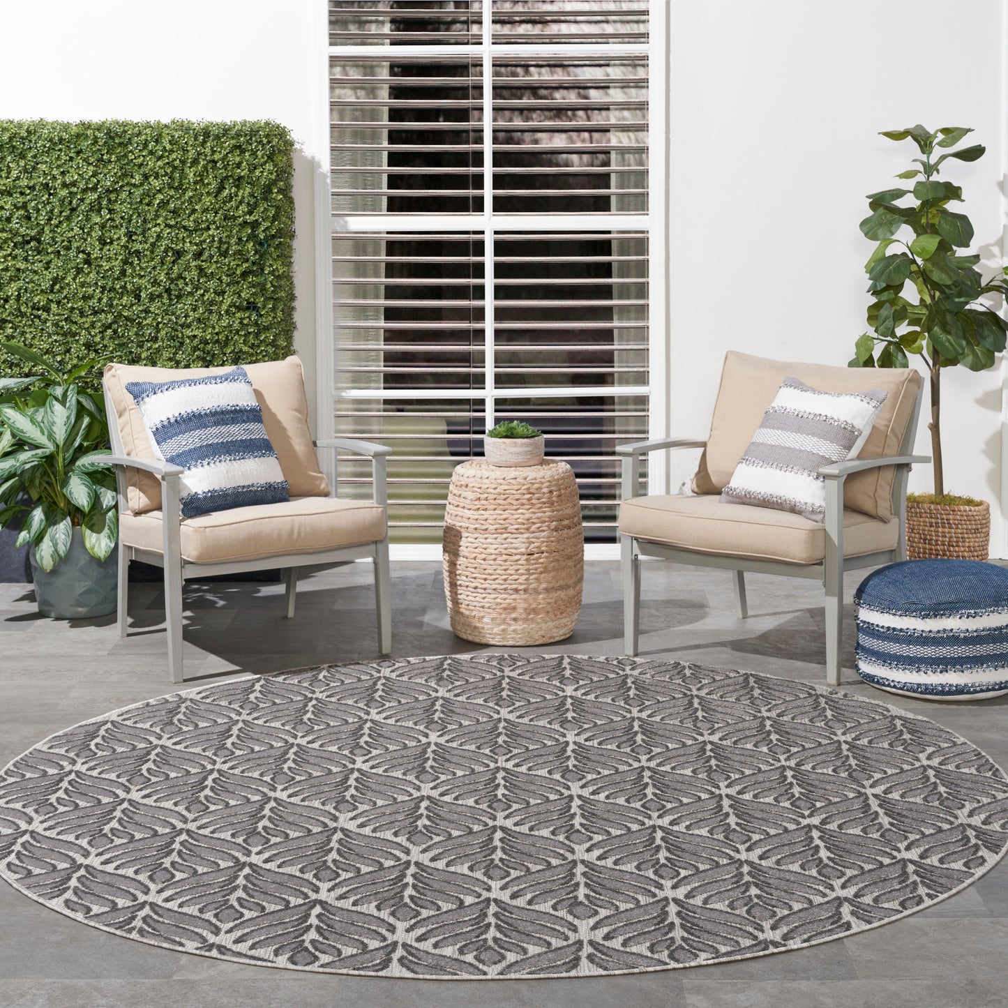 Round gray outdoor rug between two beige cushioned chairs with blue and white striped pillows and woven side table.