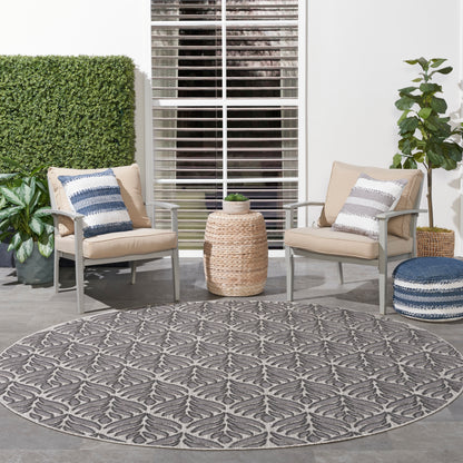 Round gray outdoor rug between two beige cushioned chairs with blue and white striped pillows and woven side table.