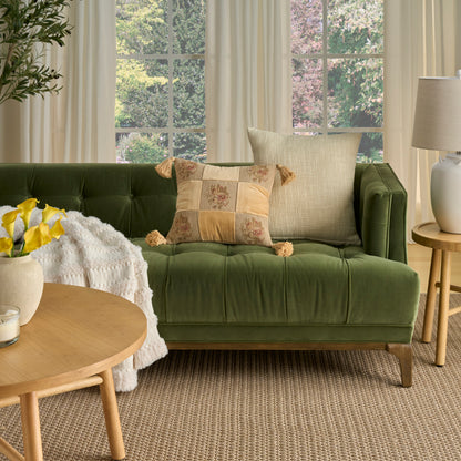 Green tufted sofa with beige cushions, cream throw, round wooden coffee table and yellow flowers in a bright living room.