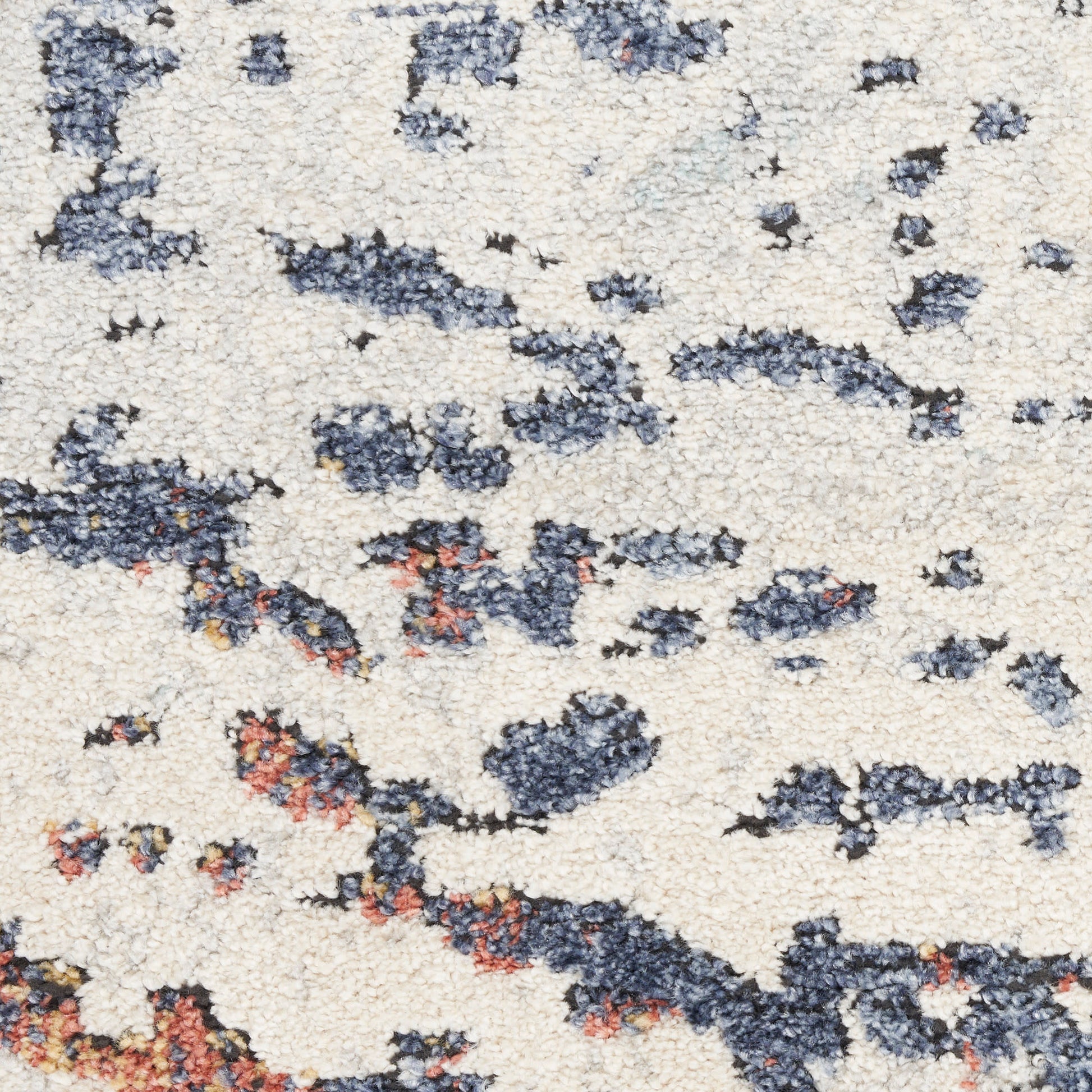 Beige shag rug with irregular navy blue and rust blotches; plush pile, abstract modern style.