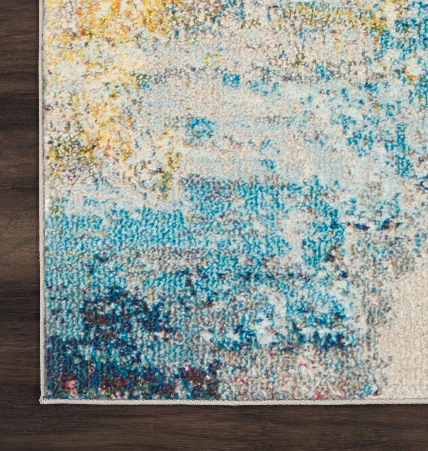 Modern abstract area rug in blue, teal & yellow on cream; textured pile, corner view on dark wood floor.