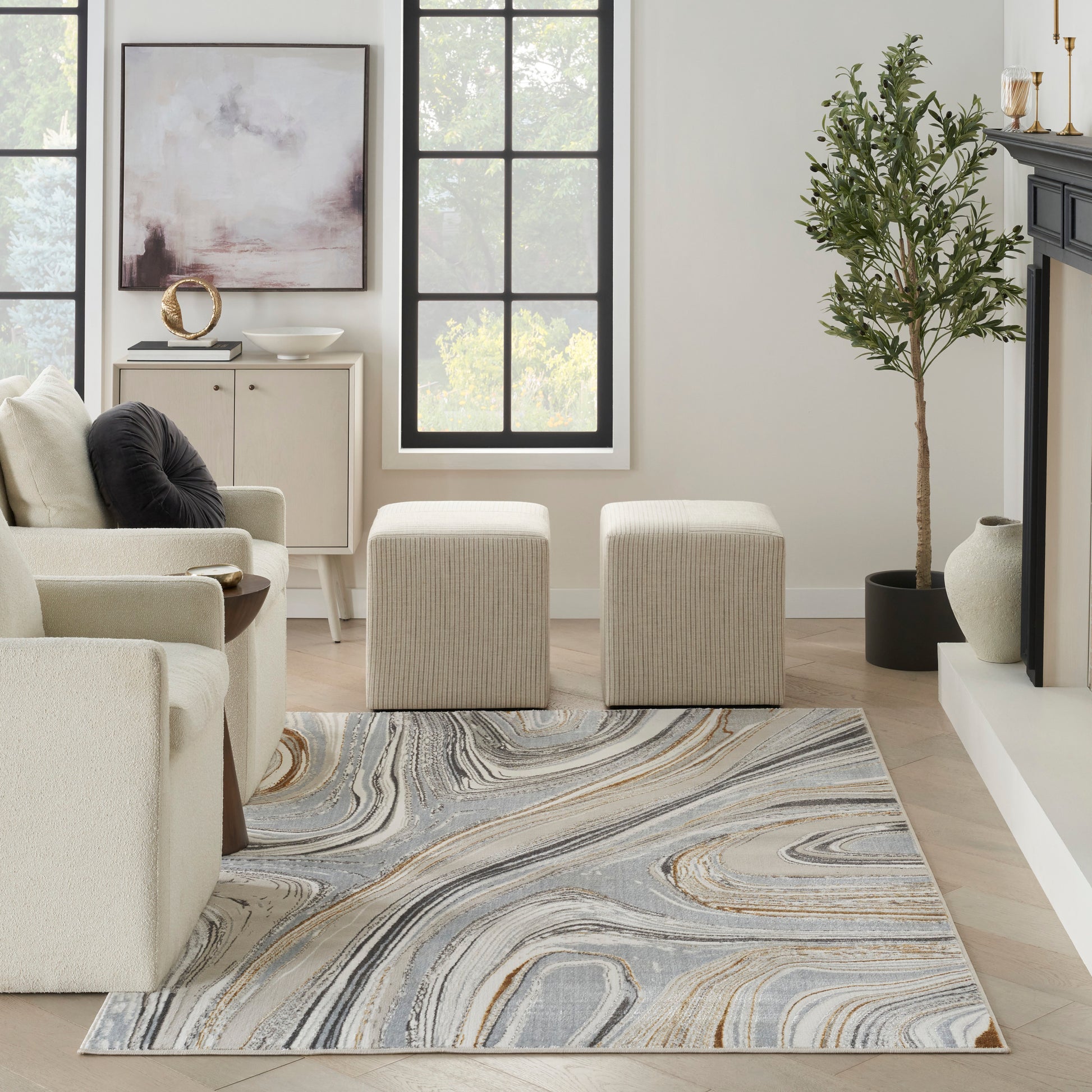 Neutral living room with cream sofa, two beige ottomans, blue-gray and tan marbled rug, black-framed windows, tall plant.