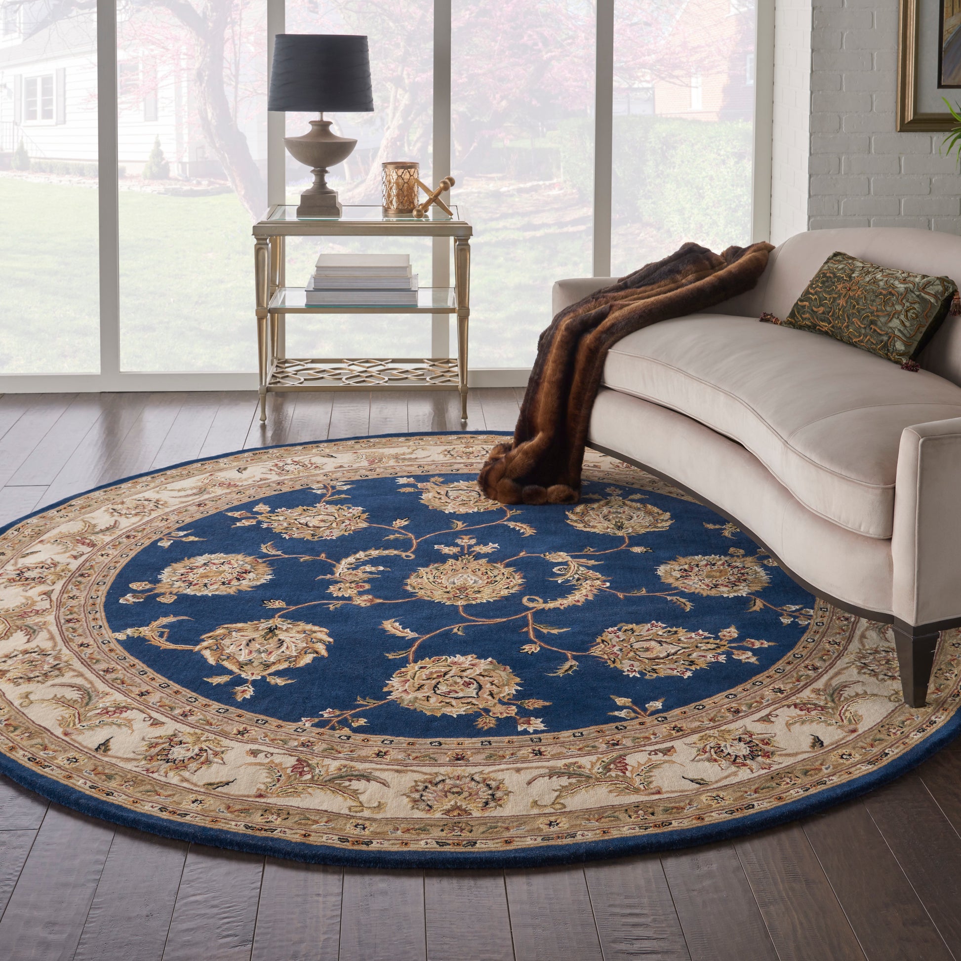 Round blue and beige oriental rug with cream floral motifs under a beige sofa and metal side table in a sunlit living room