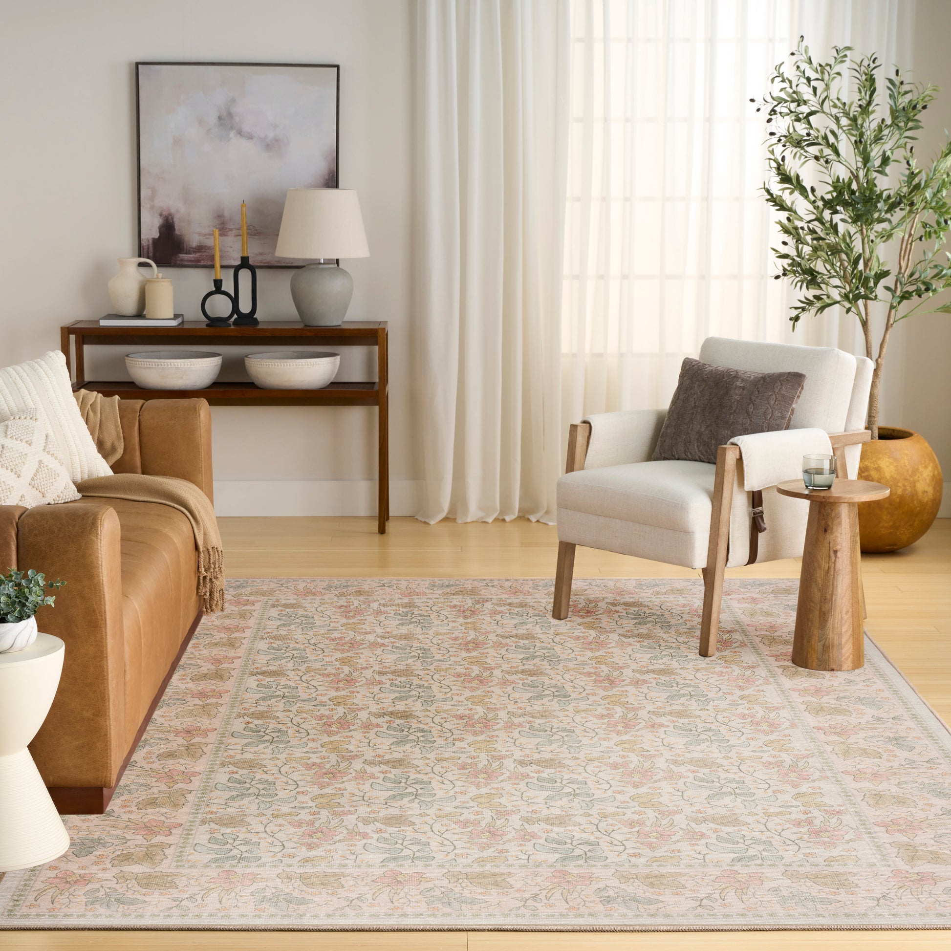 Neutral living room with beige rug, brown leather sofa, white armchair, wood console, candles, plant, sheer curtains.