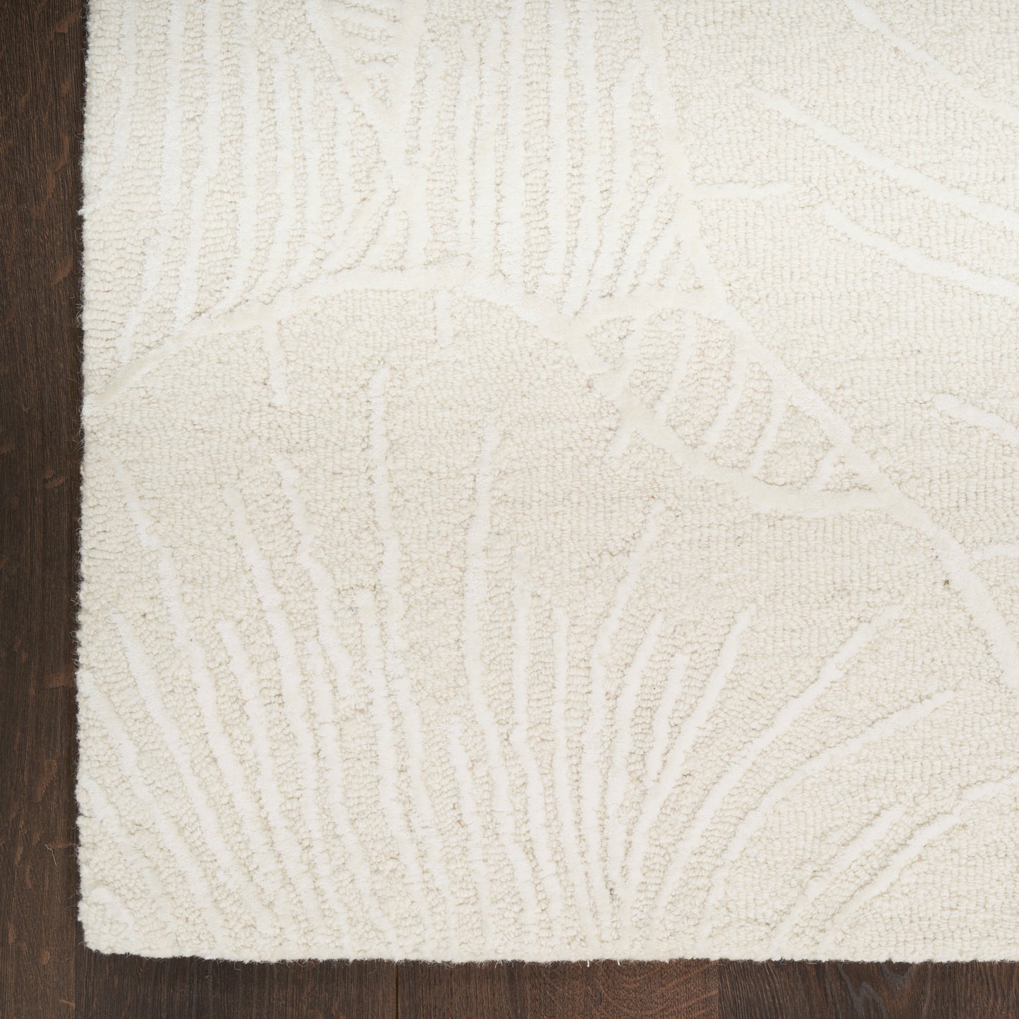 Cream tufted area rug with subtle raised leaf pattern on dark wood floor.