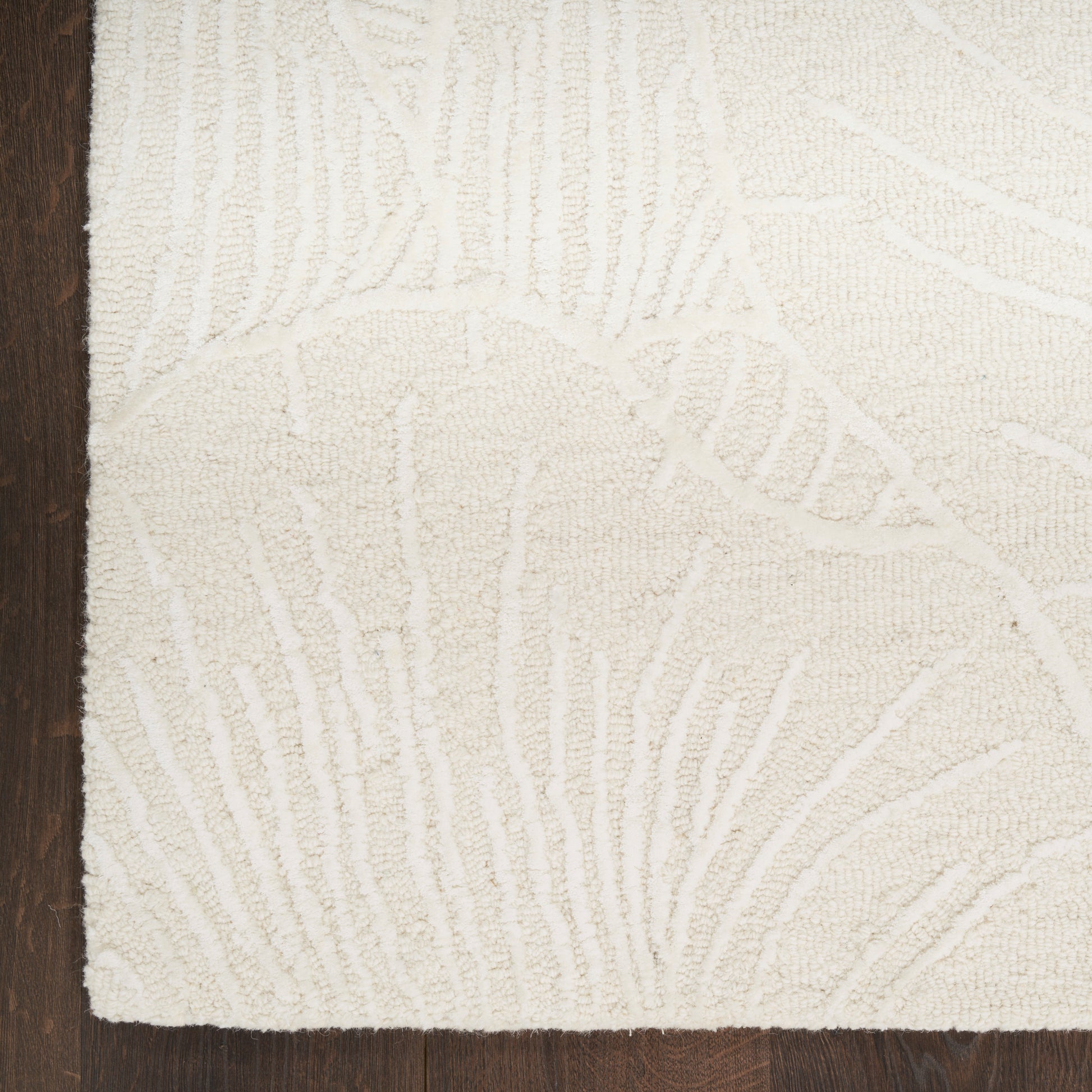 Cream tufted area rug with subtle raised leaf pattern on dark wood floor.