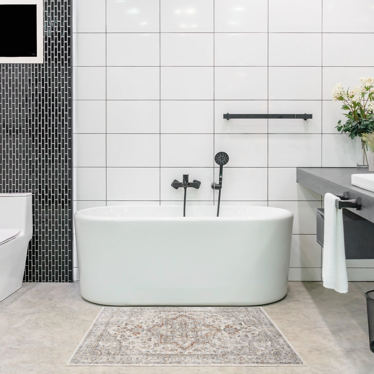 White freestanding oval bathtub with black matte fixtures in a modern bathroom; white wall tiles, black tile column.