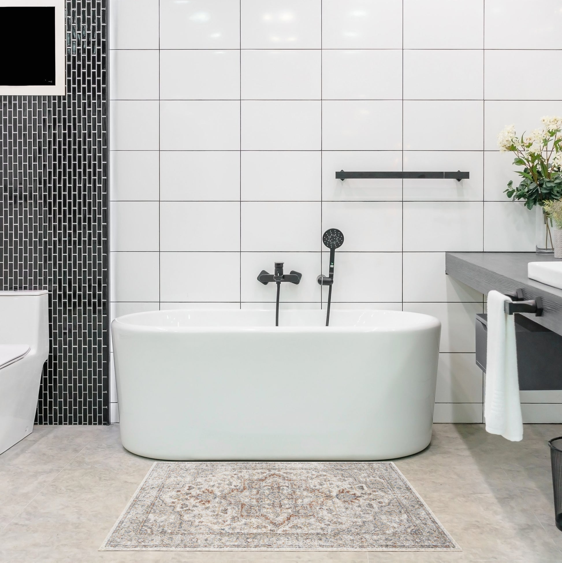 White freestanding oval bathtub with black matte fixtures in a modern bathroom; white wall tiles, black tile column.