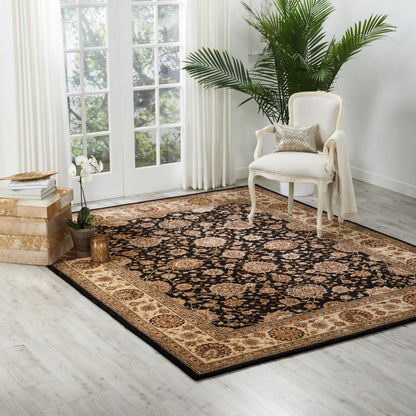Persian-style area rug with black field and tan-gold border; white upholstered armchair, potted plants, light wood floor.