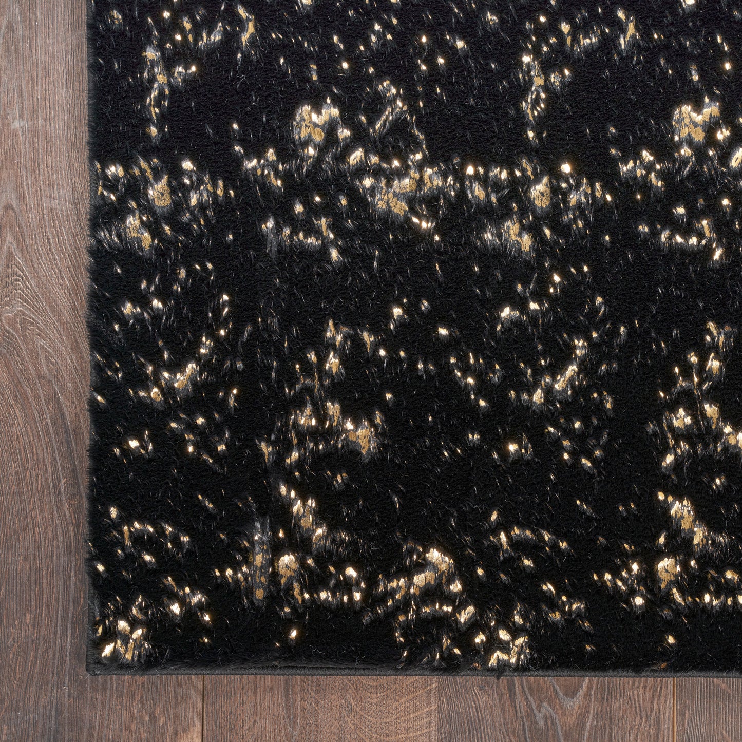 Black shag rug with gold metallic flecks, plush pile and visible edge binding on wooden floor.