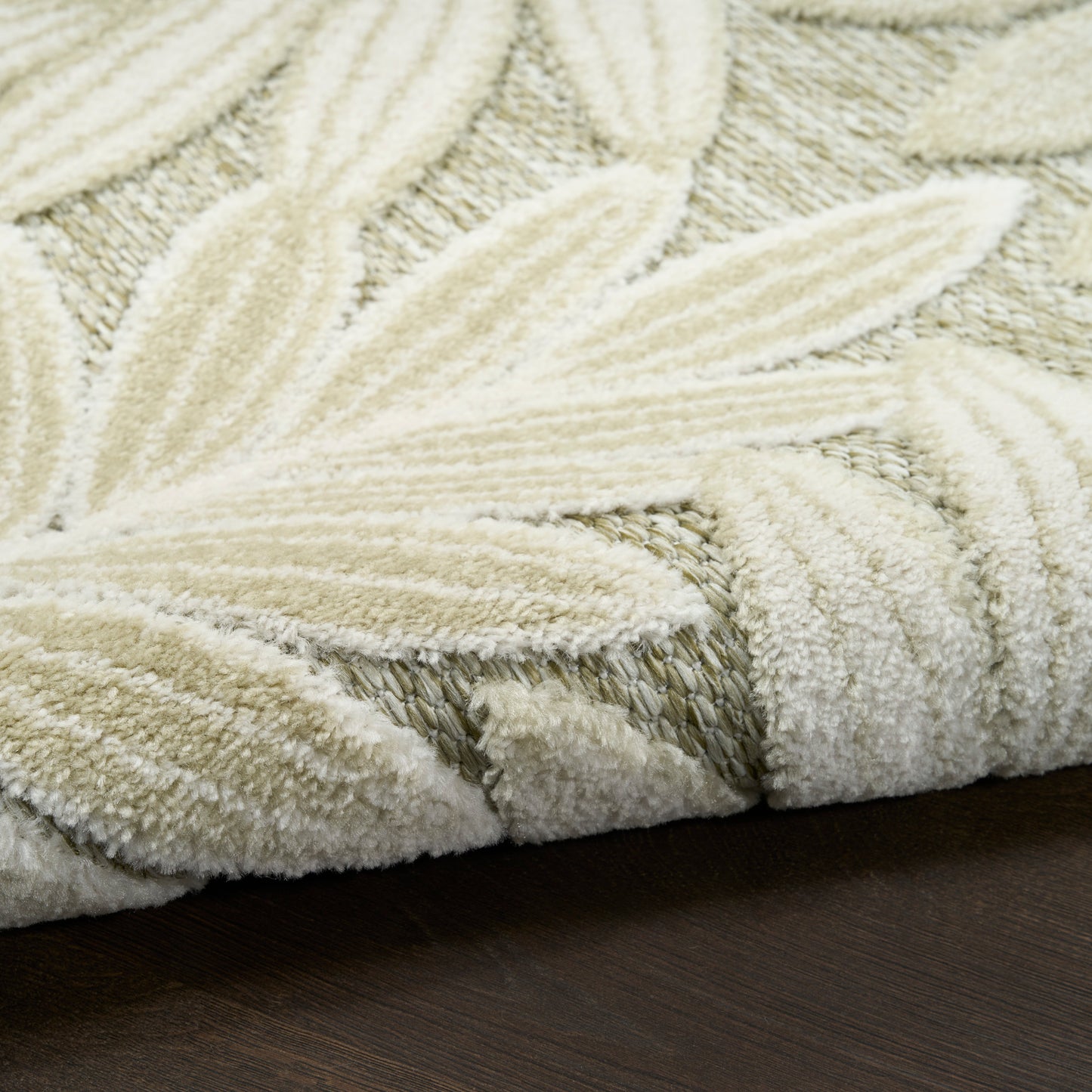 Ivory shag rug with a raised leaf motif and plush texture on a dark wooden floor.