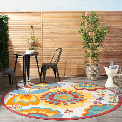 Outdoor patio with round colorful floral rug, black metal chairs, small table, hanging plant, by a wooden fence.