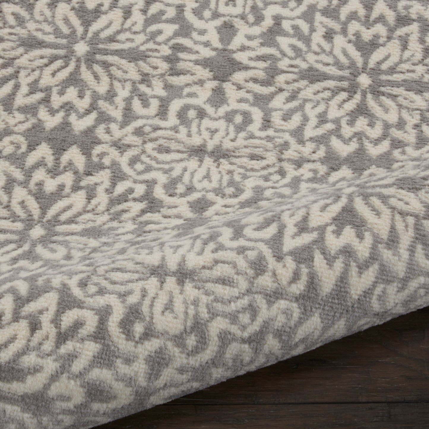 Gray and ivory ornate floral patterned area rug with plush pile on dark wood floor.