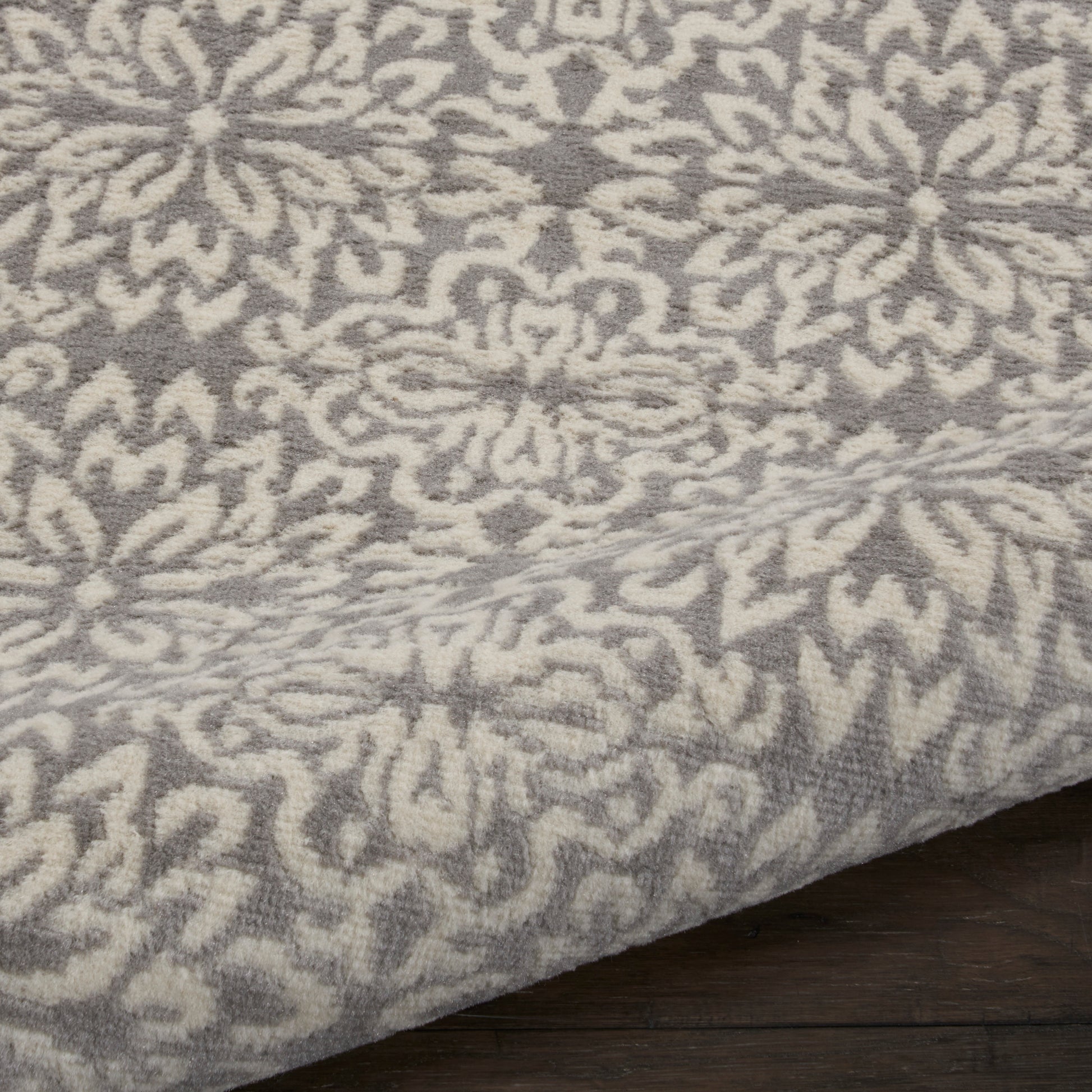 Gray and ivory ornate floral patterned area rug with plush pile on dark wood floor.