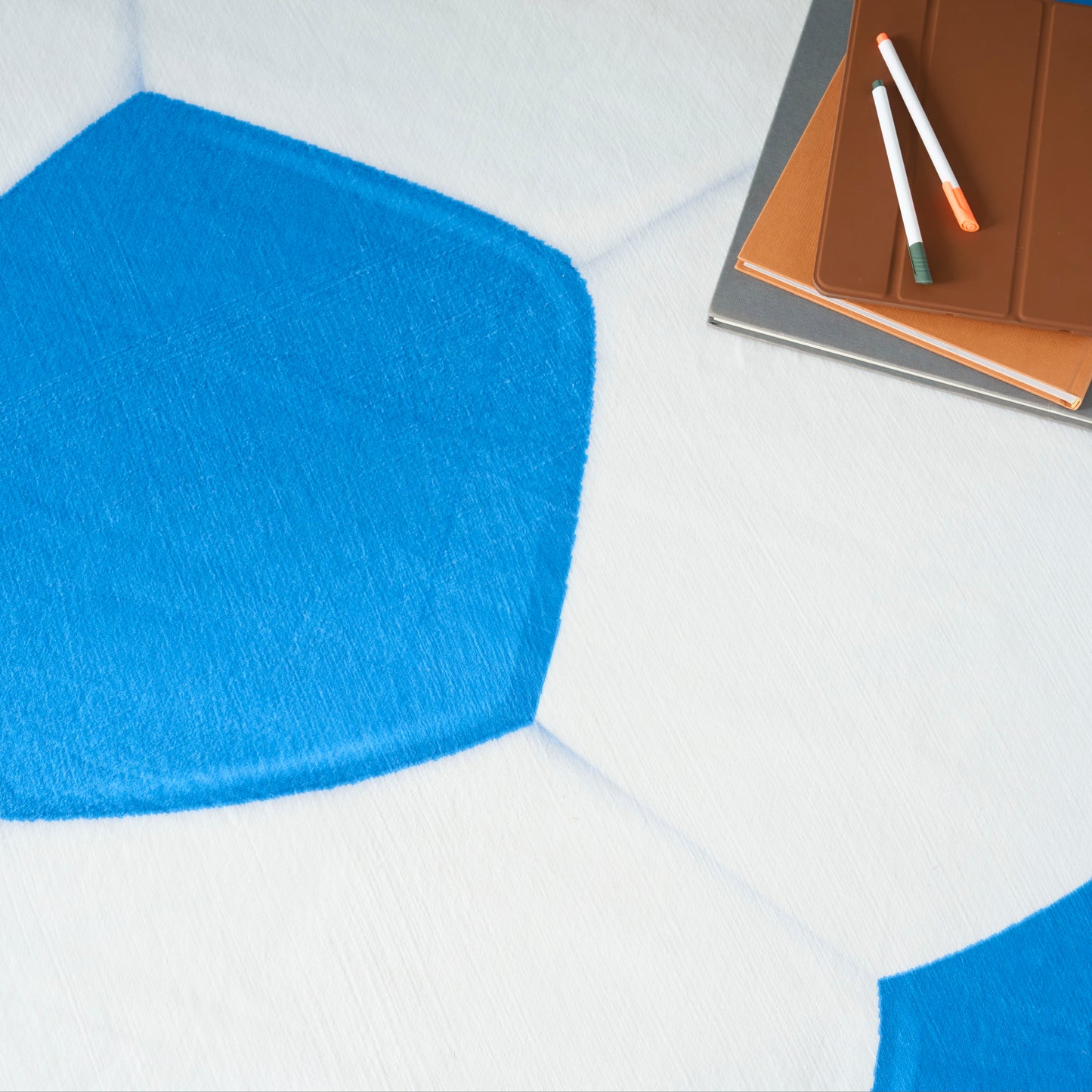 Blue geometric rug on a white floor with a brown notebook and colored pencils resting in the corner.