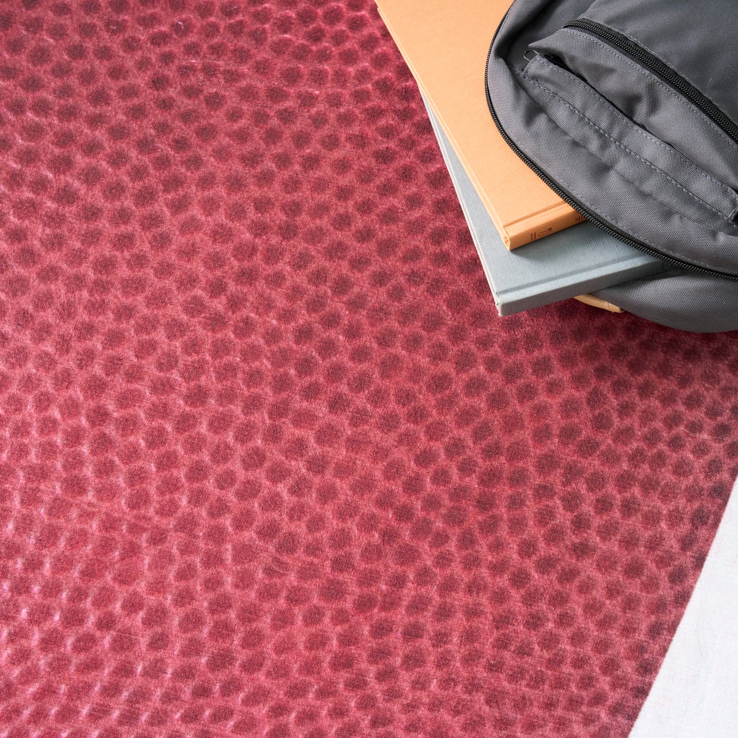 Red pebble-textured fabric background with a gray zippered pouch atop orange and blue notebooks.