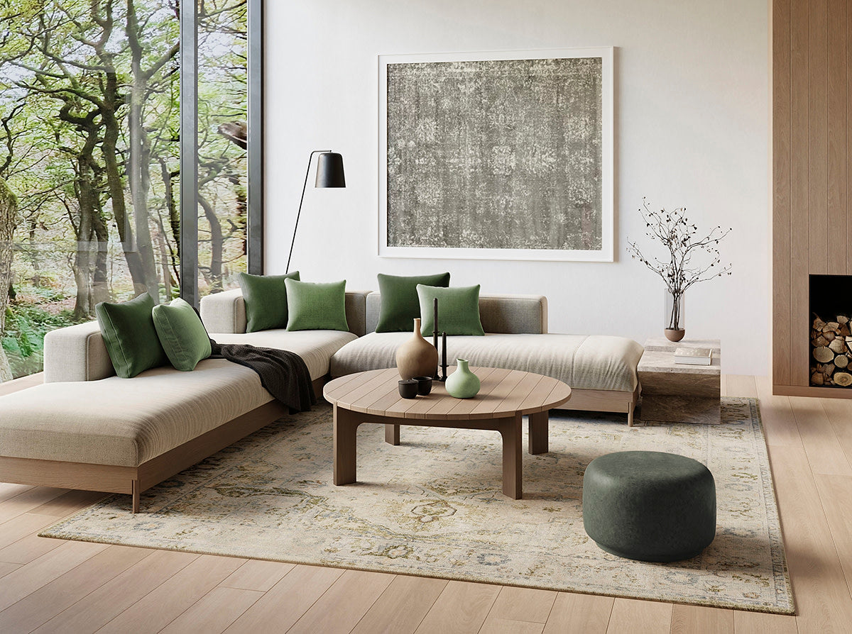 Modern living room with beige L-shaped sofa, green cushions, round wooden coffee table, green pouf, large window, rug.