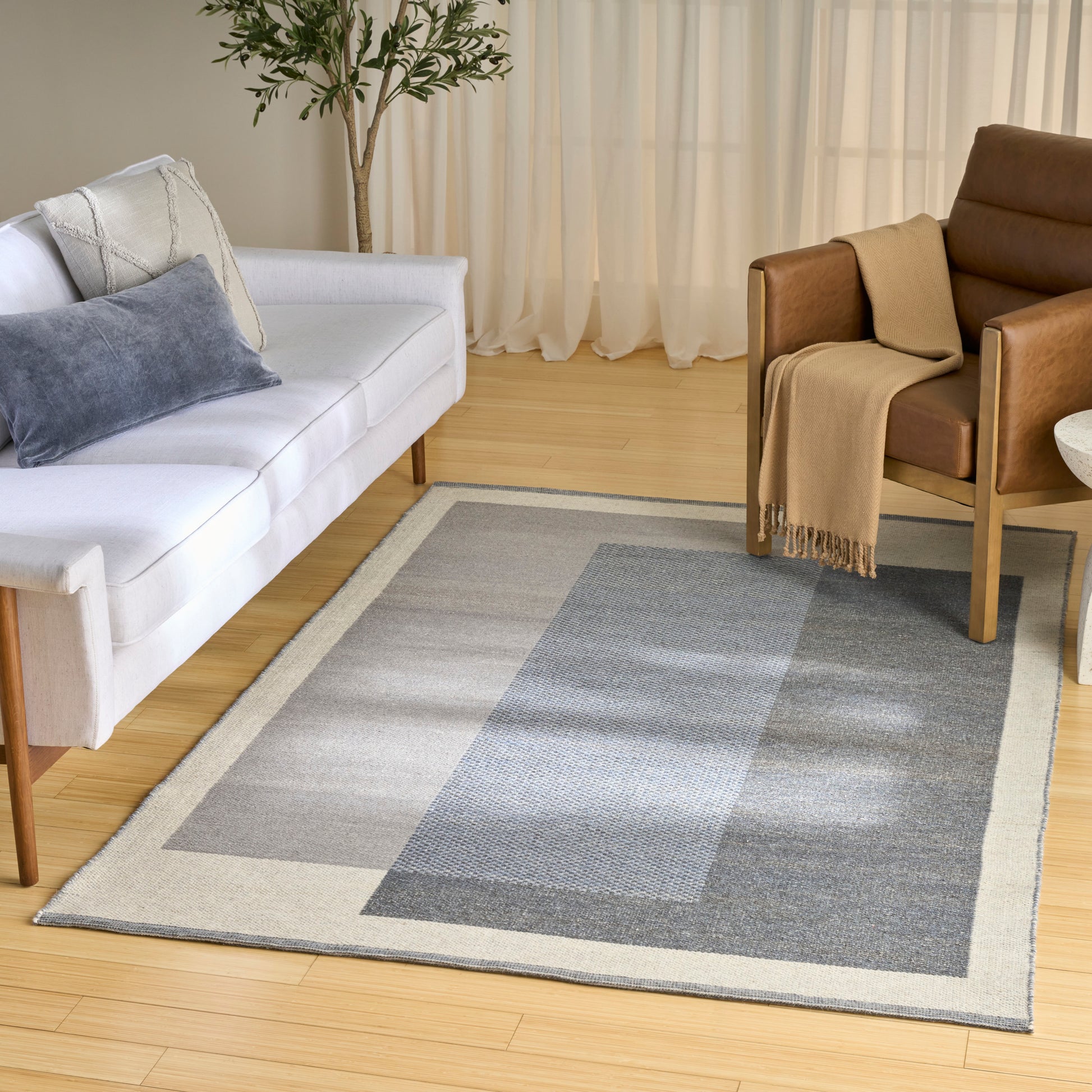 Geometric grey-beige area rug in a modern living room with white sofa, brown armchair, light wood floor.