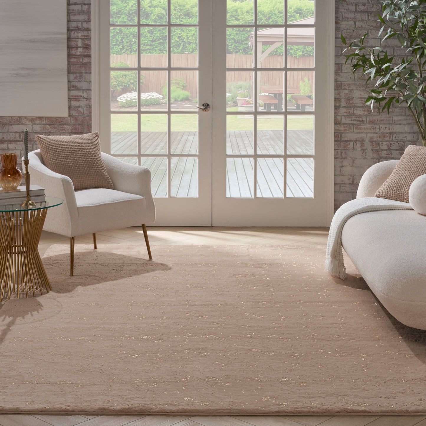 Neutral-tone living room with white upholstered armchairs, beige area rug, brick walls and French doors to a deck.