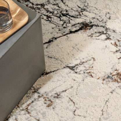 Cream marble-pattern rug with brown veining, 4' x 6', under a grey concrete rectangular block with a light wood tray and a glass on top.