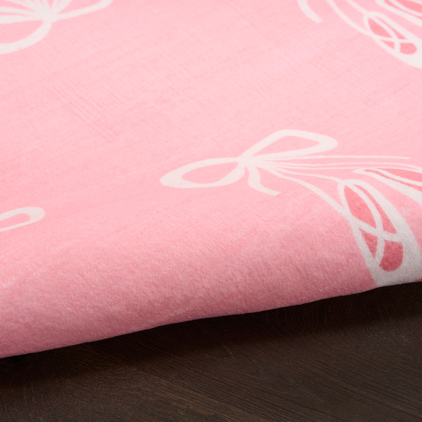Soft pink rug with white bow motifs, 7' x 9', folded on a dark wooden surface.
