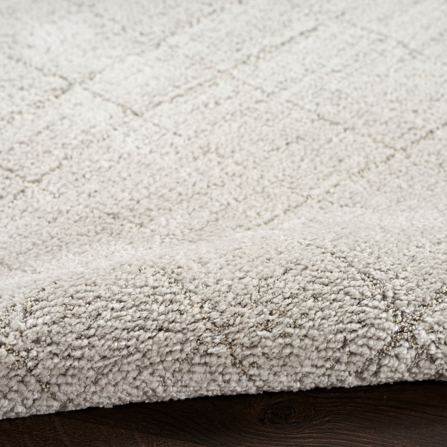Beige textured rug with a subtle diamond lattice pattern and rolled edge on dark wood floor.