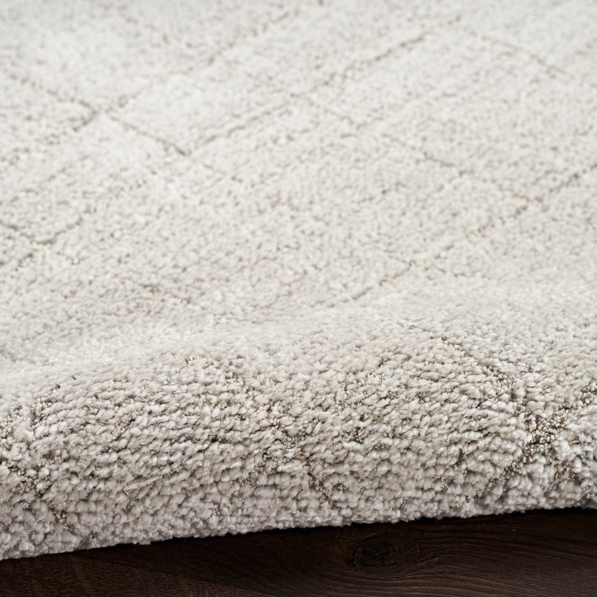 Beige textured rug with a subtle diamond lattice pattern and rolled edge on dark wood floor.