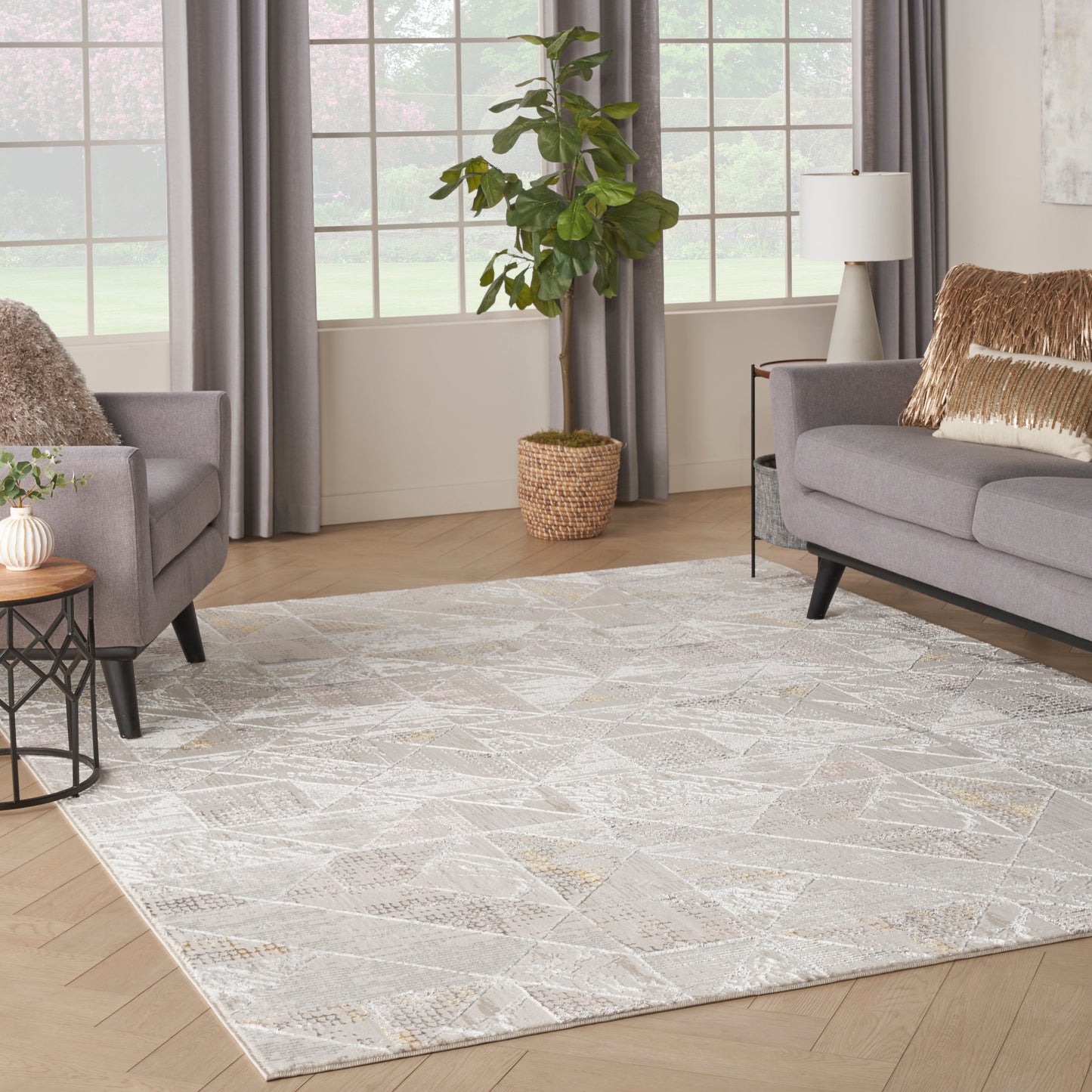 Bright living room with a large pale geometric rug, gray sofas, fur throws, and a potted plant in a wicker basket.
