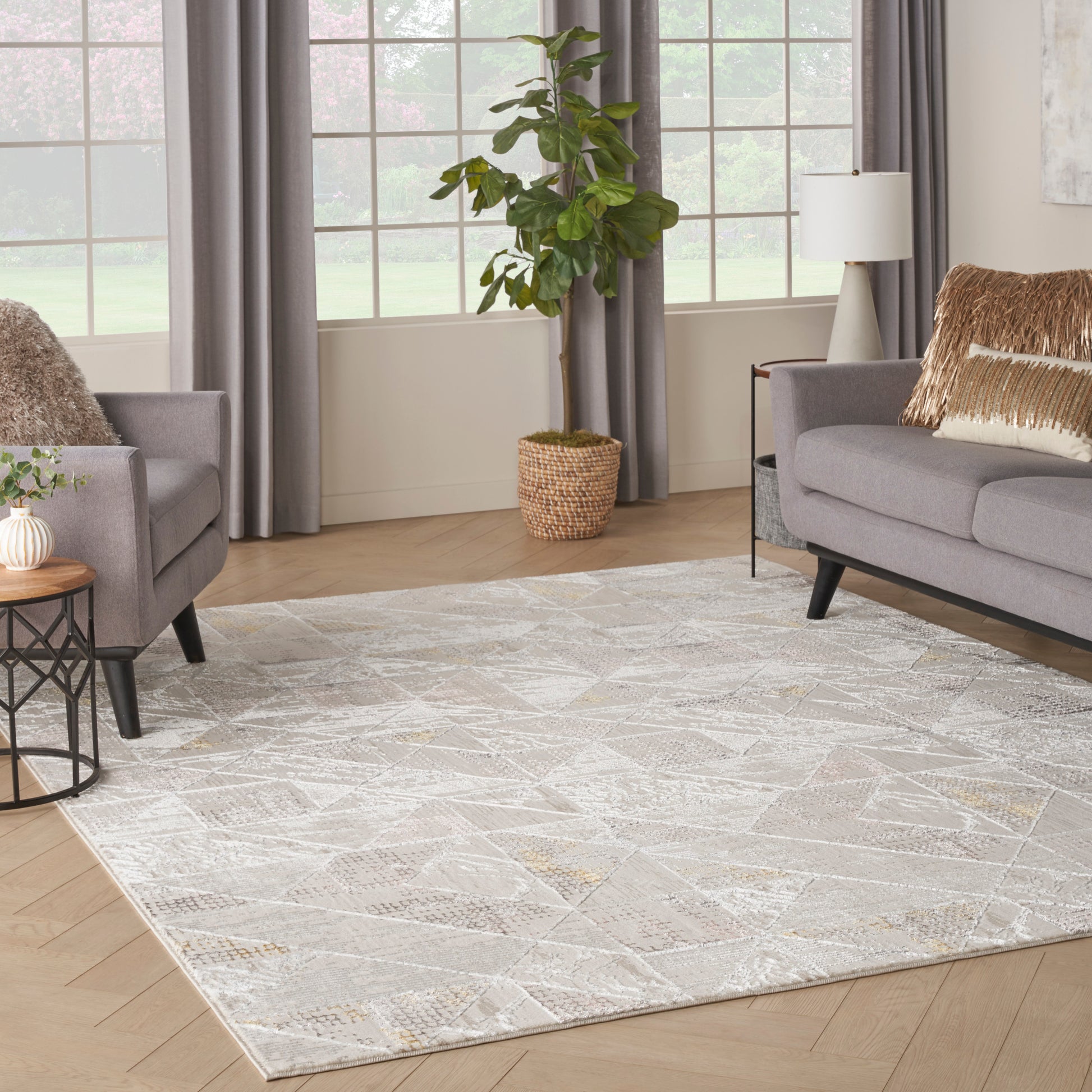 Bright living room with a large pale geometric rug, gray sofas, fur throws, and a potted plant in a wicker basket.