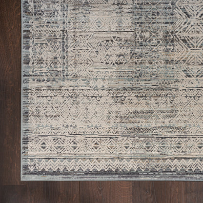 Blue-gray distressed geometric rug with tribal motifs and white accents, laid on dark wood flooring.