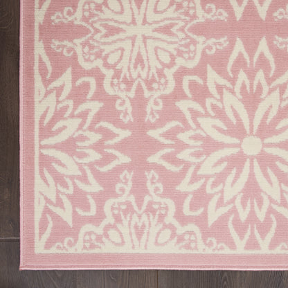 Rectangular pink area rug with white damask floral pattern and pale pink border on dark wood floor.