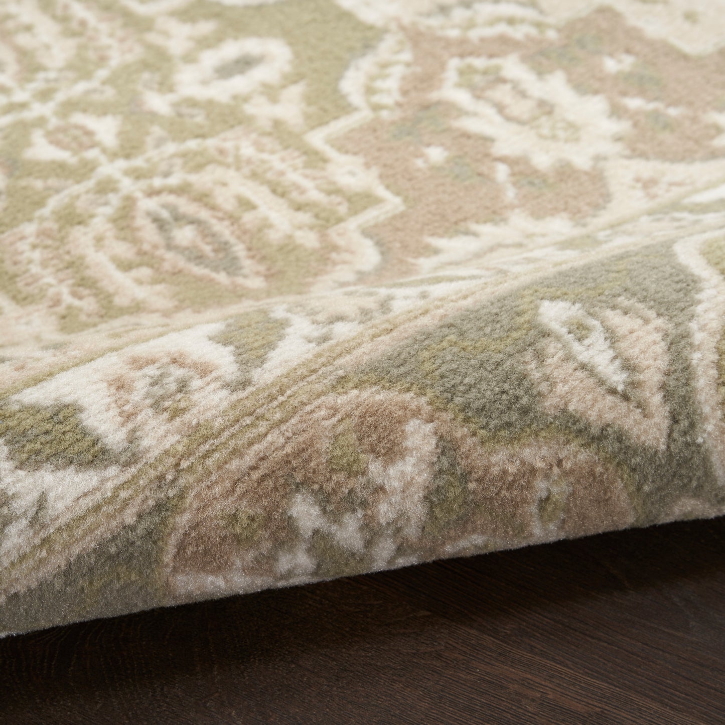 Close-up of a beige oriental-style rug with cream and taupe patterns, folded edge on a dark wood floor