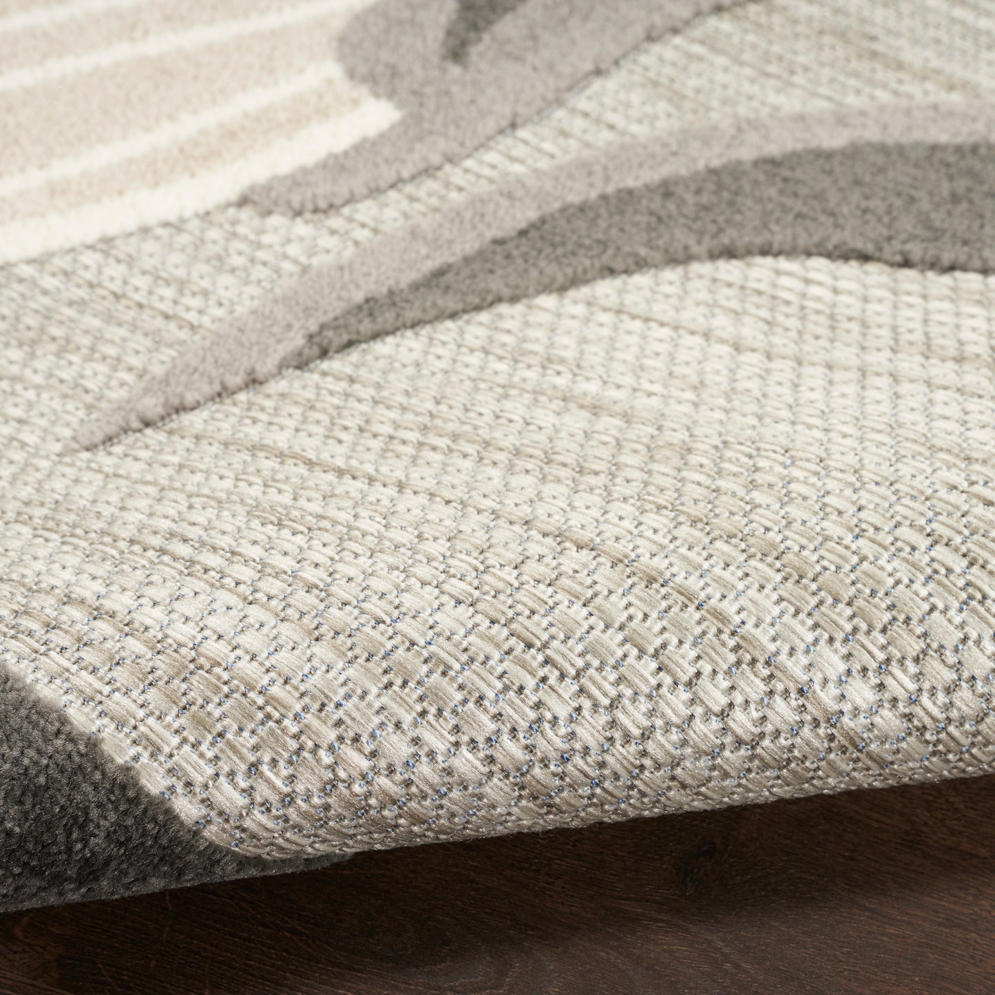 Close-up of a neutral beige-taupe woven area rug with an abstract curved motif on a dark wood floor.