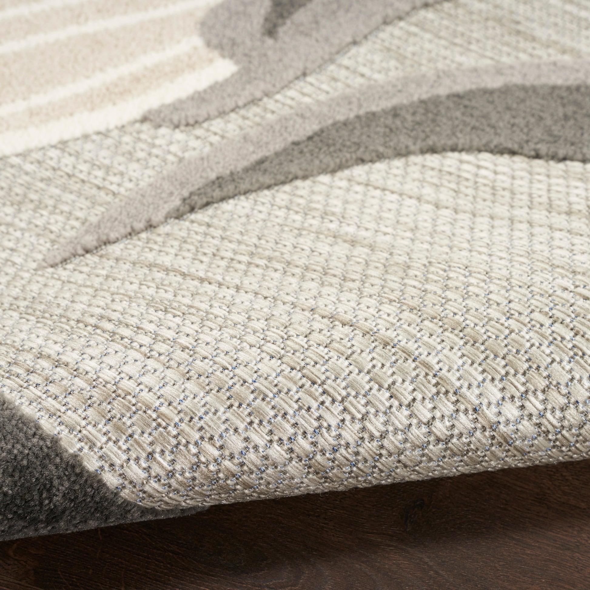 Close-up of a neutral beige-taupe woven area rug with an abstract curved motif on a dark wood floor.