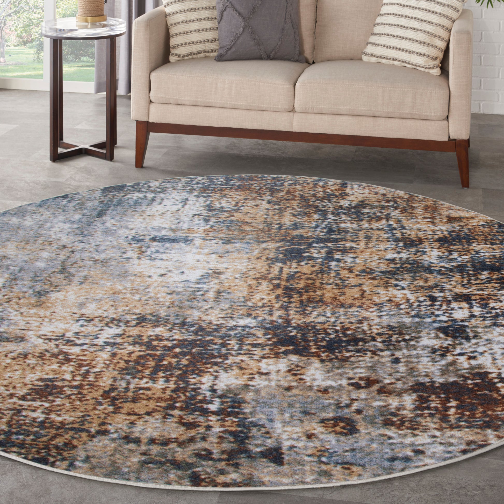 Round abstract area rug in blue, tan and brown; modern living room with beige sofa and wooden legs.