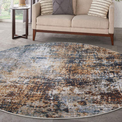 Round abstract area rug in blue, tan and brown; modern living room with beige sofa and wooden legs.