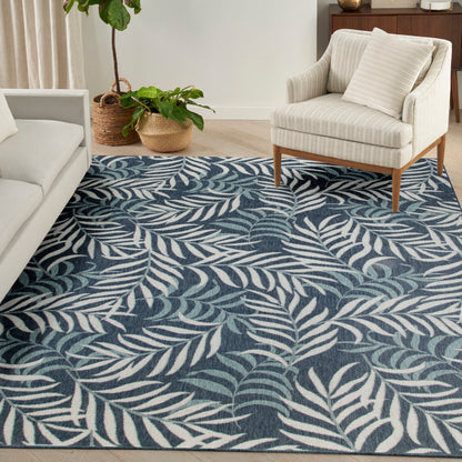Blue area rug with white palm leaf pattern in a neutral living room with a cream sofa, beige armchair and wooden accents.
