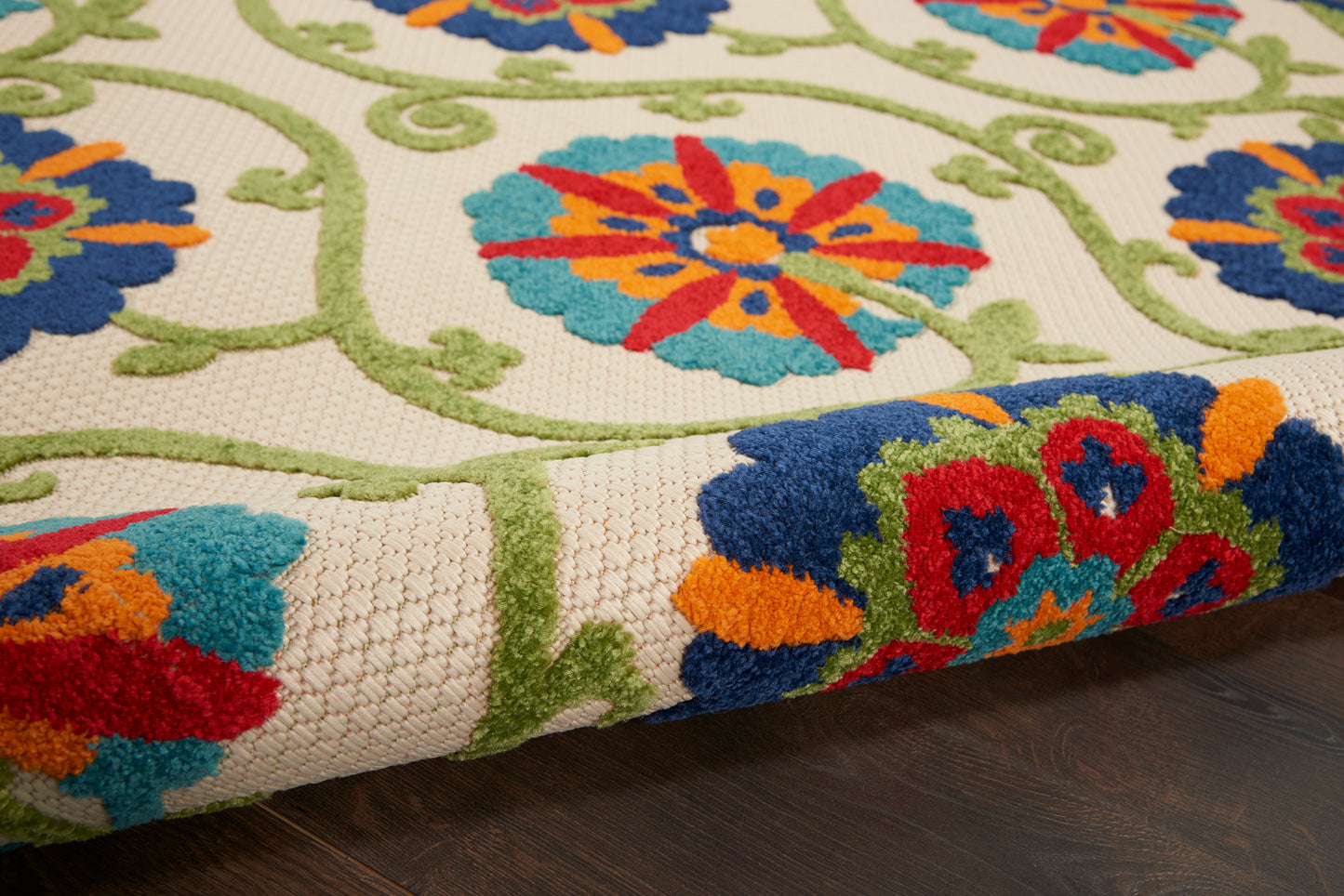Close-up of cream woven rug with bright floral pattern in orange, blue, turquoise and red with green vines; folded edge.