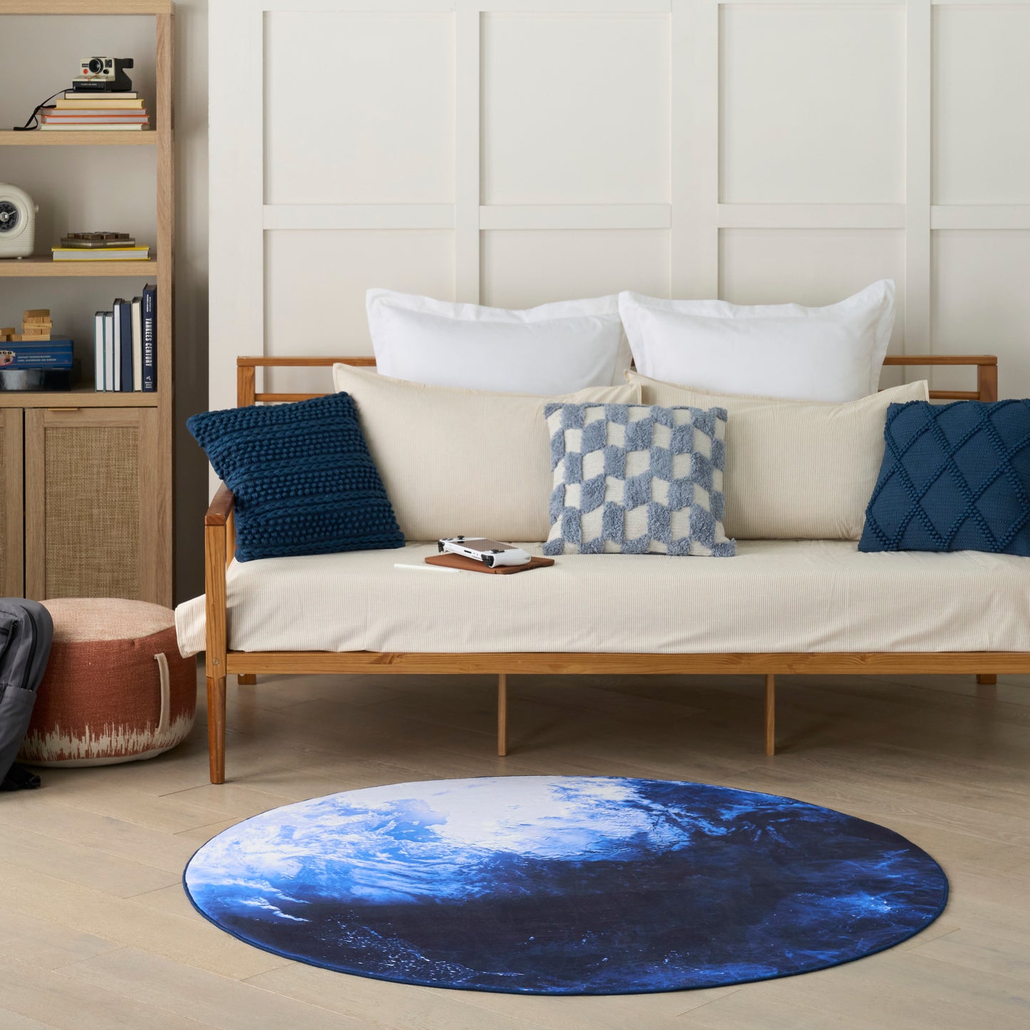 Round blue Earth-pattern rug on light wood floor, beige sofa with white pillows and navy cushions in a cozy living room.