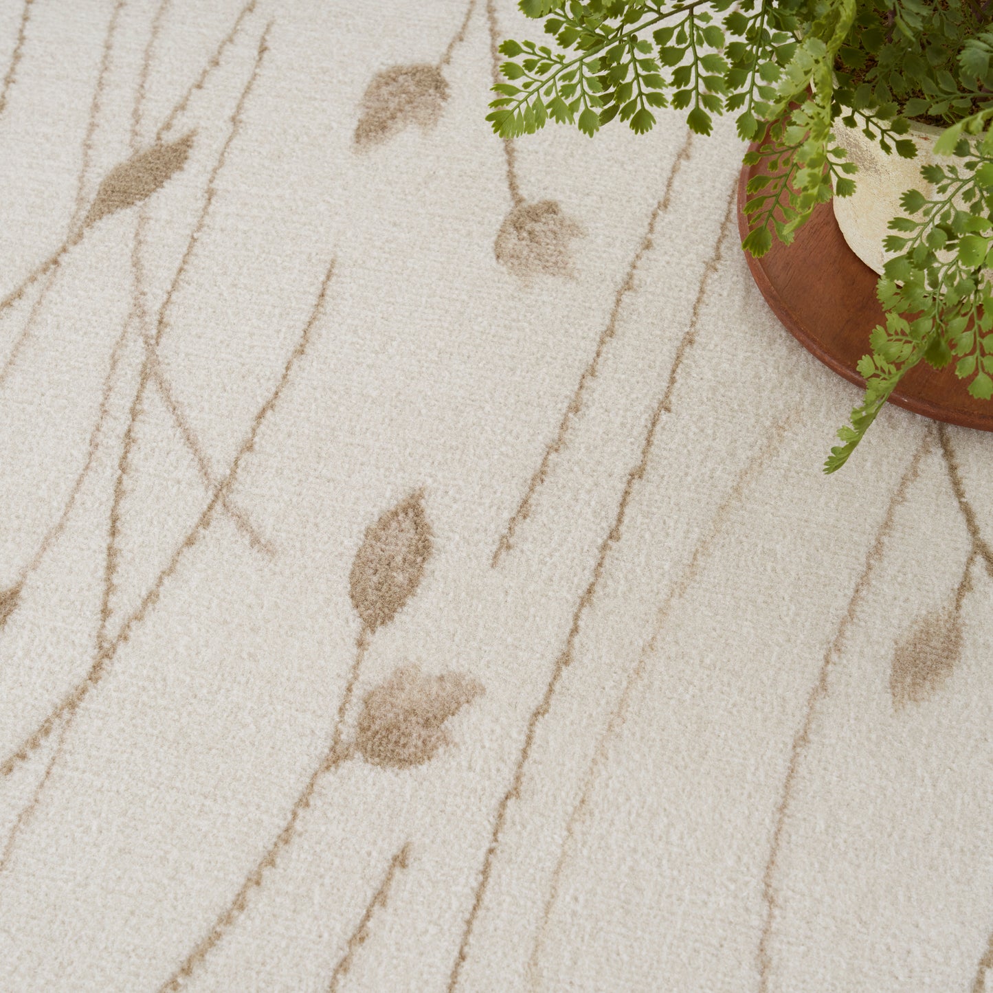 Cream textured rug with light brown leaf and branch pattern; potted fern on a wooden tray nearby.