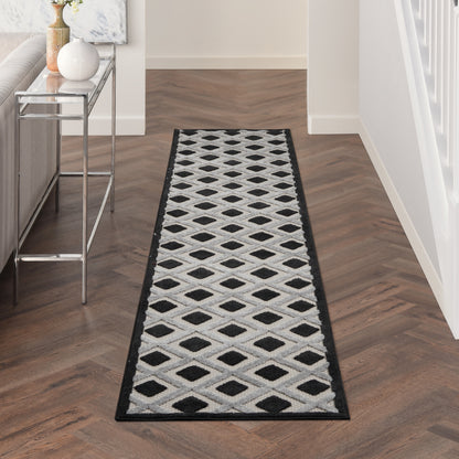 Long hallway runner rug with white and black diamond lattice pattern and black border on dark wood floor.