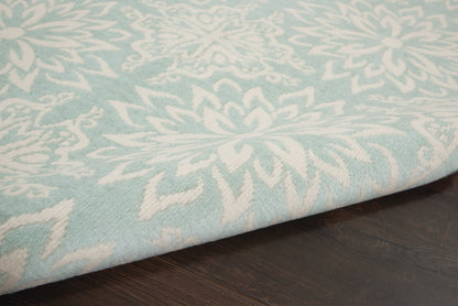 Light blue area rug with white floral pattern and thick pile, folded edge resting on dark wooden floor.