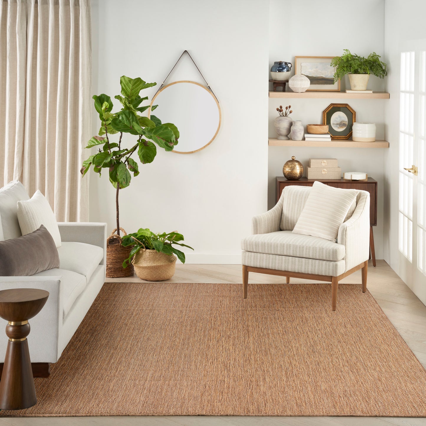 Cozy neutral living room with beige sofa, striped armchair, jute rug, tall fiddle-leaf fig, hoop, and wooden shelves.