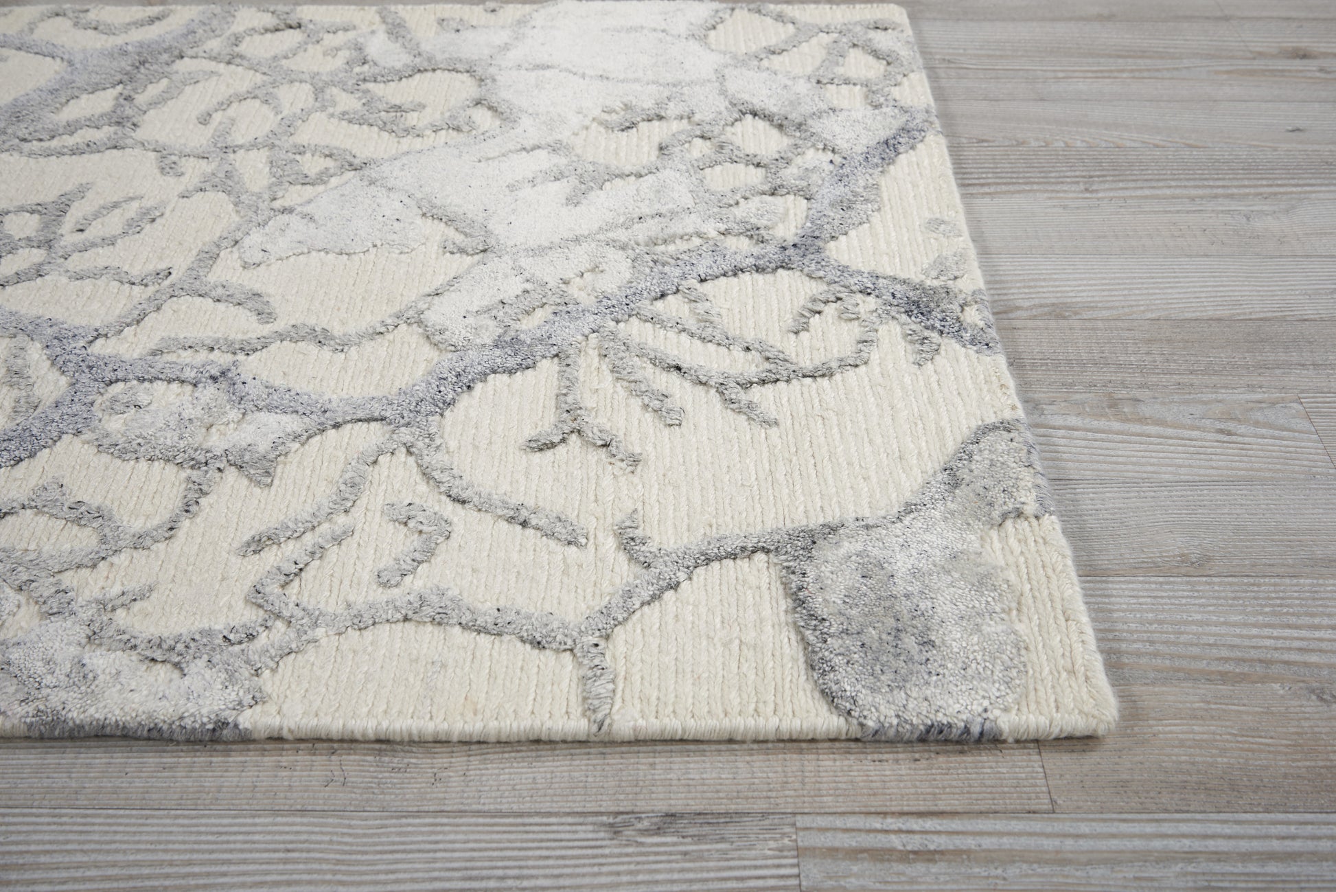 Cream rug with gray abstract branch pattern and plush texture on light wood flooring.