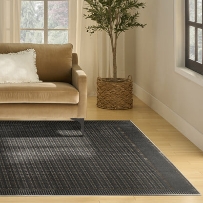 Beige sofa with white pillow, dark bordered geometric rug, and potted olive tree in a woven basket.