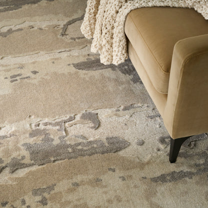 Beige upholstered sofa with black legs, draped chunky cream knit throw, atop a beige-gray abstract patterned rug.