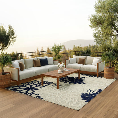 Outdoor wooden-framed sectional with beige cushions, navy pillows, coffee table, potted plants, and a blue floral rug.