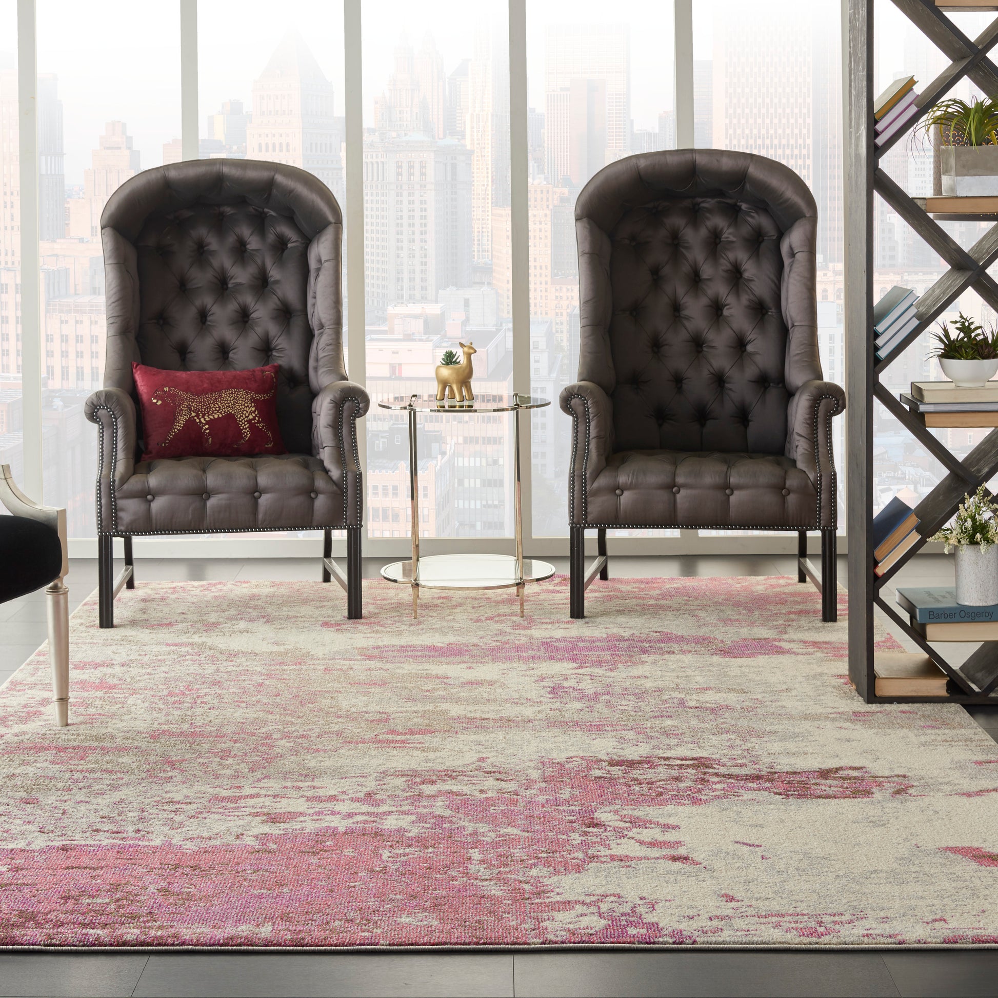 Pair of dark tufted leather wingback chairs with rolled arms, glass round side table, pink-beige rug, city skyline backdrop.